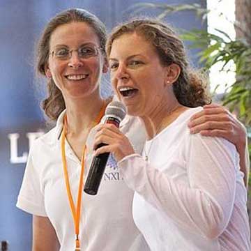 Seagram's heiresses Clare Bronfman and Sara Bronfman onstage promoting the teachings of their master, Keith Raniere. Note Clare is wearing a NXIVM shirt. Raniere has guided the sisters into commodities and real estate ventures where $100 million mysteriously disappeared. More money - has disappeared since the initial $100 million which came from a trust fund. The Bronfman's father, Edgar Bronfman Sr. died in 2013 leaving them large additional monies for Raniere's schemes.