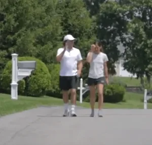 The princely [and a little tubby] Keith Alan Raniere walks with his DOS slave Daniela Padilla. One has to feel a little sorry for this young lady; she might have thought he was a noble prince but he was her cruel abuser. If she were your daughter, you might consider killing this skunk for what he did to her.