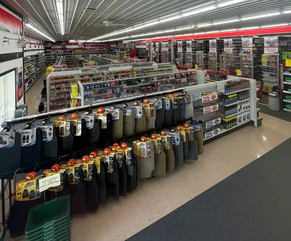 A store aisle lined with rows of car floor mats on display, with shelves of tools and auto accessories in the background.