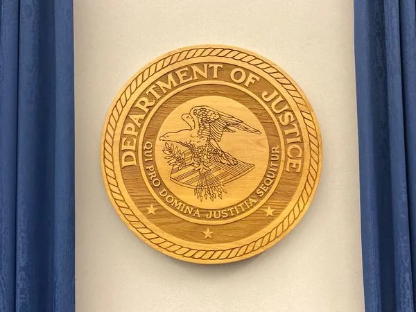 Wooden Department of Justice seal featuring an eagle in the center and a surrounding Latin motto, mounted against a neutral backdrop.