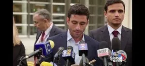 Marc Elliot addressed the media after the sentencing of Keith Raniere with Eduardo Asunsolo at his side. In the background is Frank Parlato who covered the sentencing for the Frank Report. Parlato dubbed the group of five who have been the most vocal in support of Raniere as "The Nxivm-5". At a press conference the day before, they referred to themselves as the Nxivm -5 and, with a smile, Elliot thanked Parlato for so naming them.